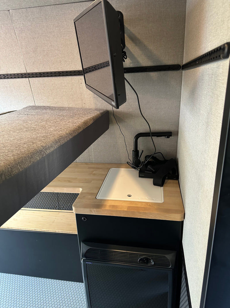 Modern RV rental interior with bunk bed, wall-mounted TV, wood counter, sink, & Engel fridge. Compact living. — photo 8