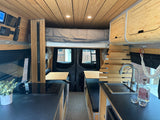 Luxurious RV rental interior: bamboo walls, kitchen, bed, and seating create a cozy, tech-equipped travel space.
