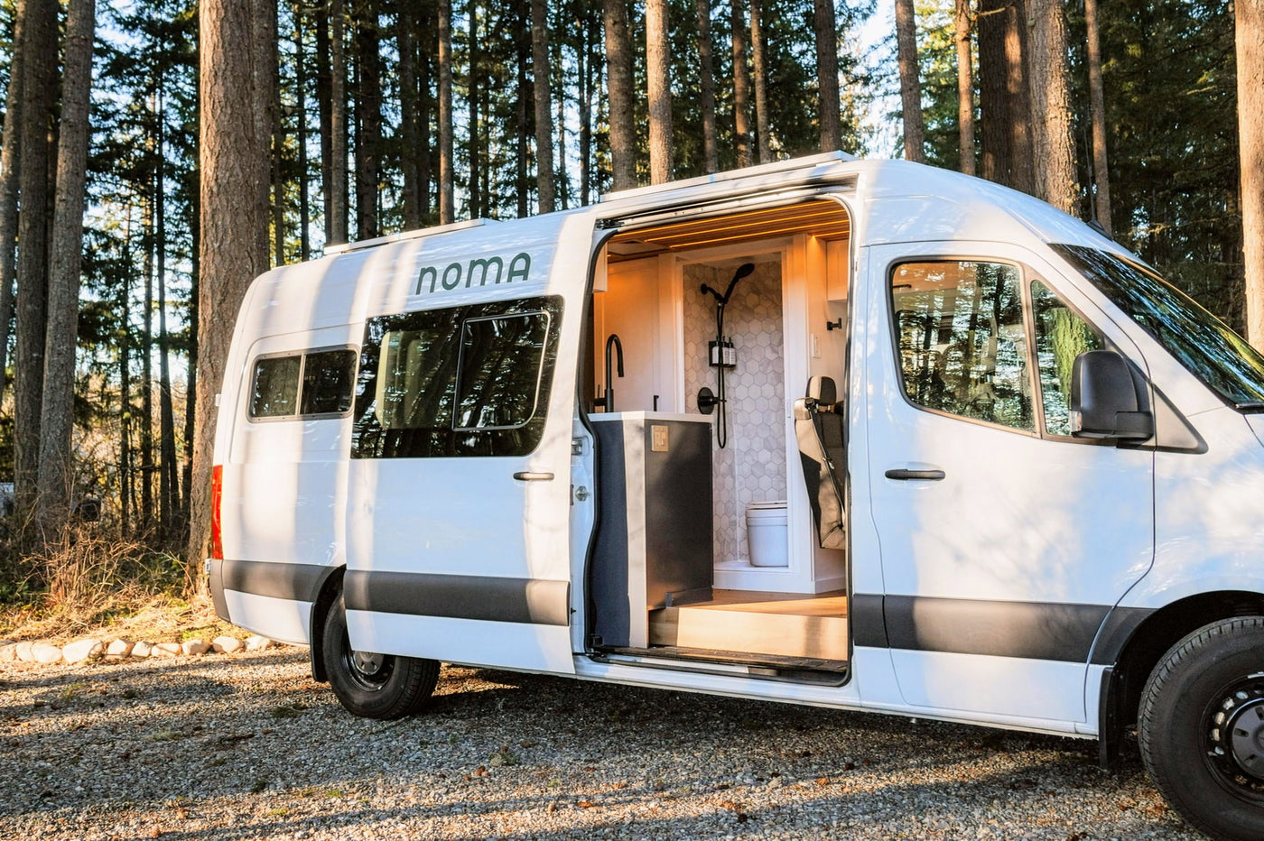 Noma rv rental parked among trees, showcasing a modern camper van interior with a sleek kitchen and shower area. — photo 10