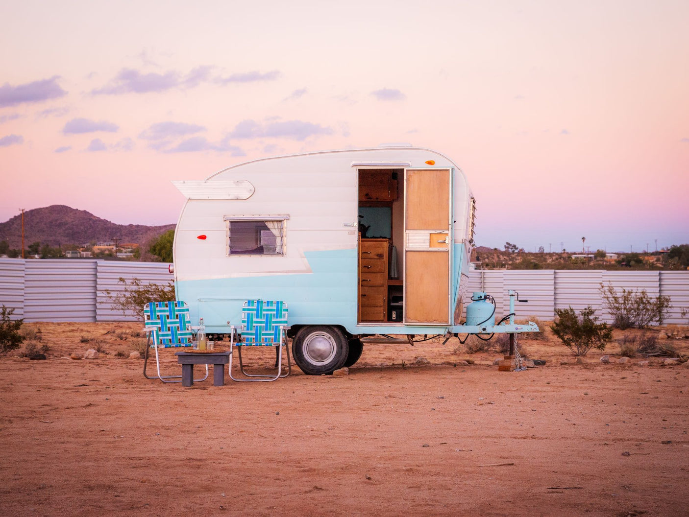 Retro RV rental parked in the desert at sunset. A vintage travel trailer with chairs outside, perfect for a peaceful getaway.