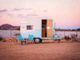 Retro RV rental parked in the desert at sunset. A vintage travel trailer with chairs outside, perfect for a peaceful getaway.