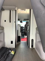 Looking through the clean interior aisle of an RV rental towards the driver's cabin, with camping gear on the floor.