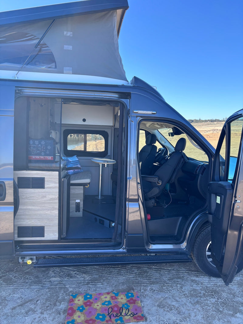 View inside a modern camper van RV rental with pop-top roof, open side door revealing kitchen, seating, and driver's cab. — photo 14