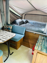 Explore this cozy RV rental's interior: comfy bed, dining nook, and "adventure" pillow. Ideal for camping trips!