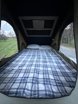 Comfortable tent bed with plaid blanket & pillows, overlooking nature. Ideal for a cozy rv rental camping adventure.