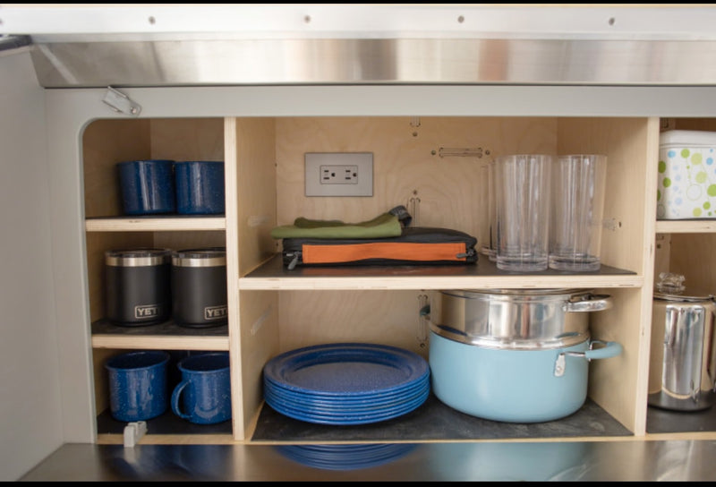 RV rental kitchen storage: Cookware, blue enamelware, Yeti mugs, and clear glasses neatly arranged in wood cabinets. — photo 10