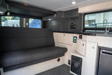 RV rental interior: a dark grey sofa, light wood cabinetry, modern kitchen with sink, and digital control panels are visible.