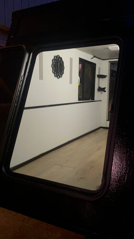 A clean, minimalist RV rental interior is visible through a dark-framed window, featuring white walls, wood floors, and subtle decor.
