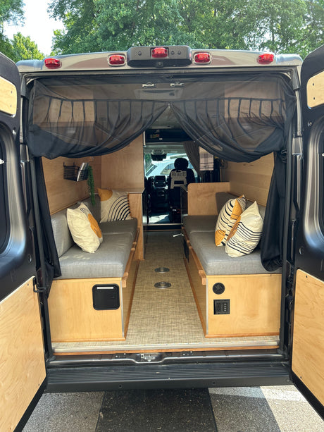 Inside a modern RV rental: wood-paneled interior with comfy benches, power outlets, and a bug screen at the rear. Ready for adventure.