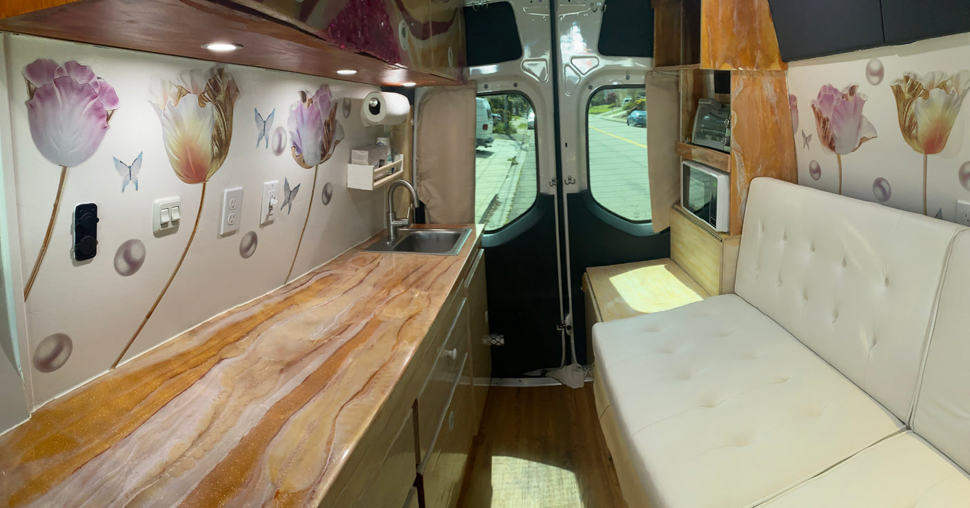 Spacious RV rental interior. Features a custom kitchen with unique gold-swirl counter, sink, appliances, and cozy sofa.