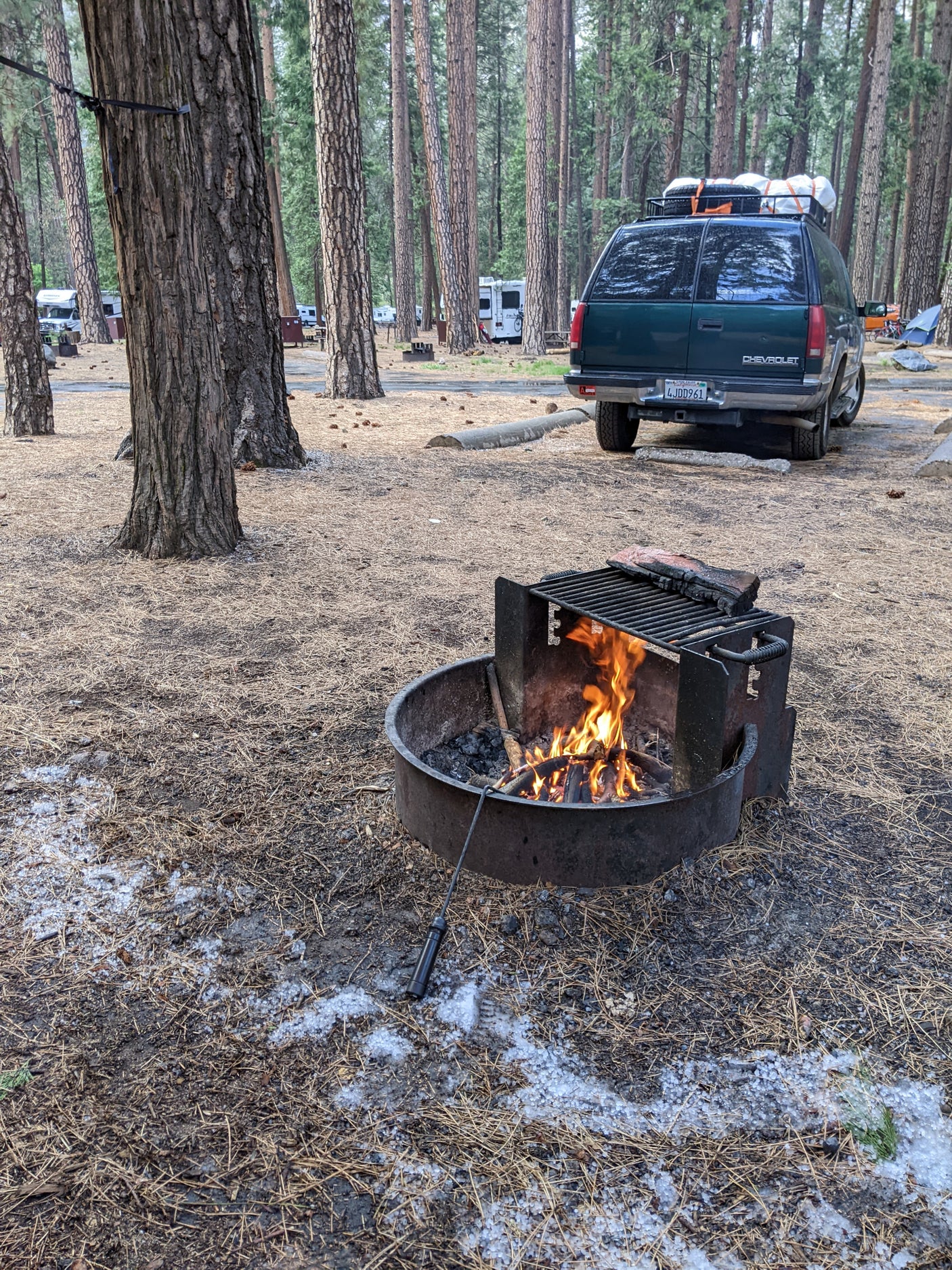 Fireside comfort at a forest campground, featuring a van, RV rentals, and fresh hail on pine needles.
