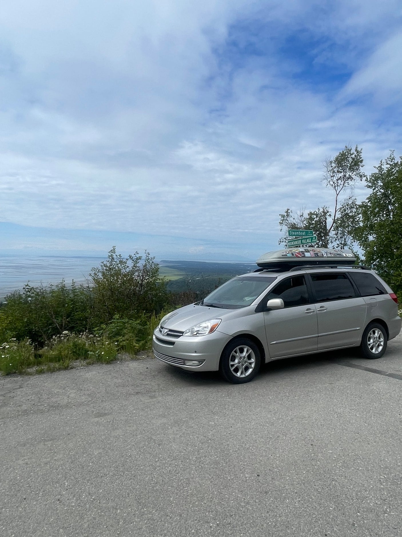  suggesting an RV rental area.|Creative car camping setup. See inside this RV rental alternative with a bed & camp stove pulled from the open tailgate.|Silver minivan with a sticker-covered cargo box