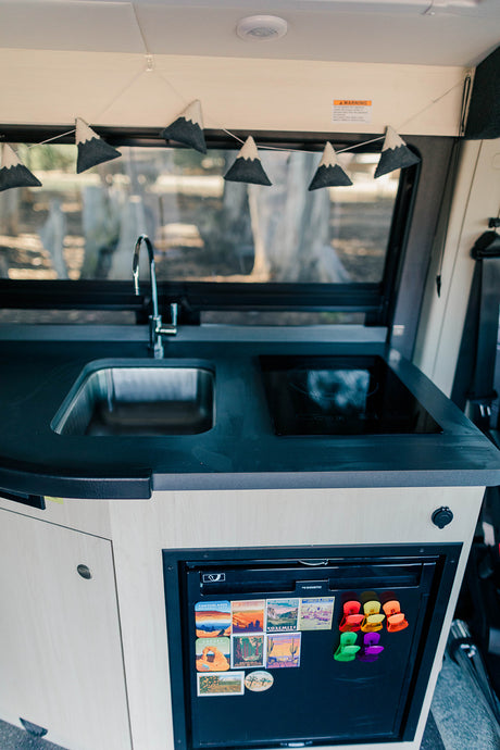 Inside an RV rental: a modern kitchen with a sink, induction cooktop, and refrigerator adorned with vibrant travel magnets.