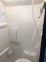 RV rental wet bath showing shower hose, toilet fixture, & a wall-mounted access panel for a compact setup.
