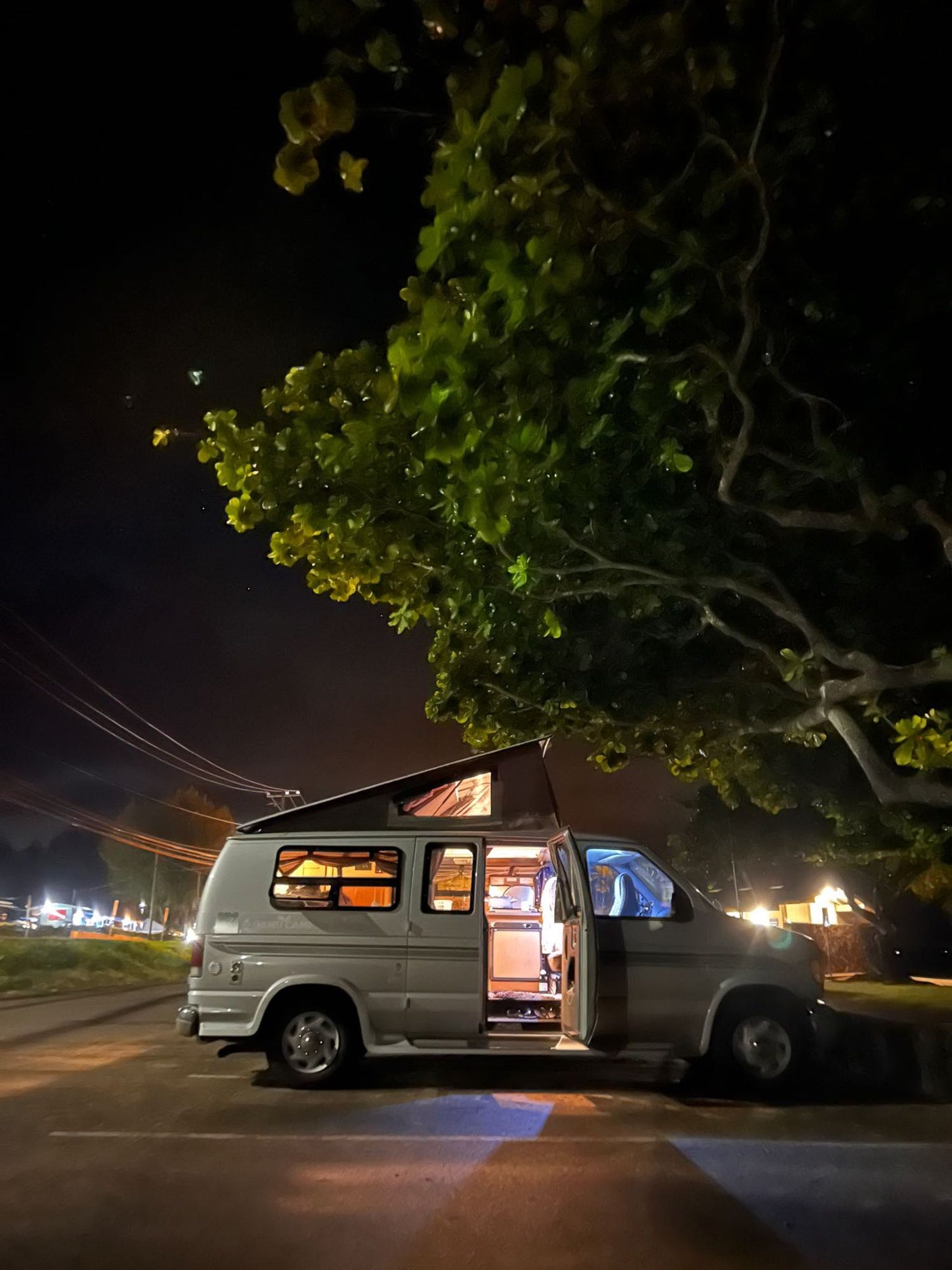An illuminated rv rental camper van, with its pop-top extended, parked at night under a tree. Ready for adventure!