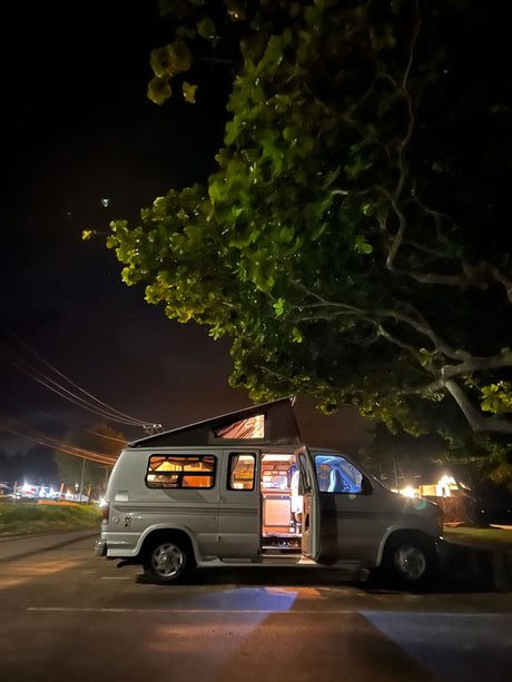 An illuminated rv rental camper van, with its pop-top extended, parked at night under a tree. Ready for adventure!