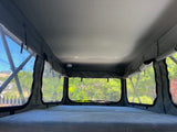 Interior of an RV rental pop-top camper with bed, clear windows looking out to nature. Includes smoke detector.