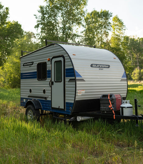 Compact Sunray Sport travel trailer RV rental in tall grass, equipped for off-grid camping adventures.