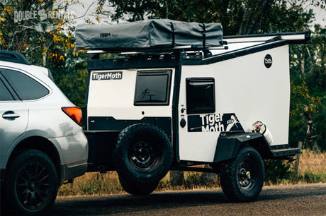 RV rental: A silver SUV tows a white and black TigerMoth off-road camper trailer with a Thule Tepui rooftop tent.