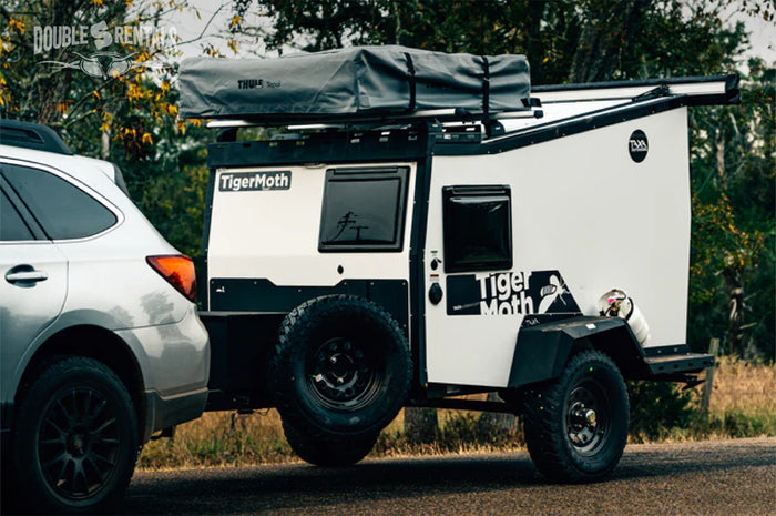 RV rental: A silver SUV tows a white and black TigerMoth off-road camper trailer with a Thule Tepui rooftop tent.