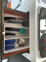Organized RV rental kitchen drawer with black spatulas, knives, and blue-handled silverware in a white organizer.