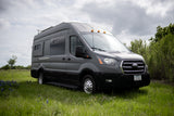 Explore with our gray Ford Transit RV rental, a versatile camper van parked in a green field.
