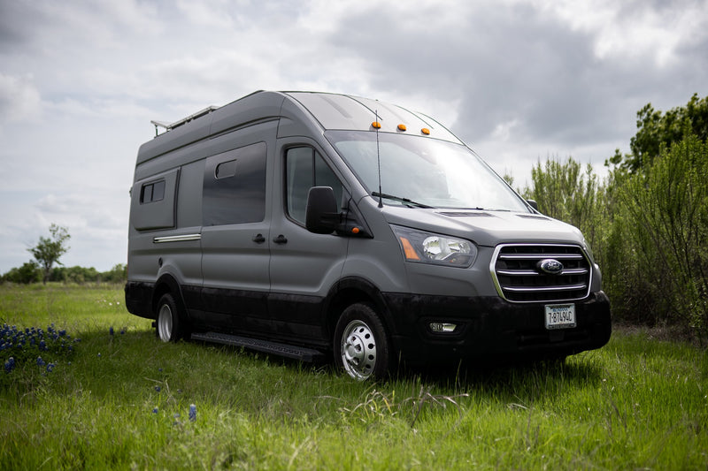  featuring solar panels and open doors revealing its cozy interior in a grassy field.|Gray Ford Transit van — photo 3