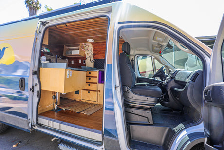 Open RV rental: a custom camper van's interior with wood paneling, counter, and driver's cabin visible, plus a mountain mural on its exterior.