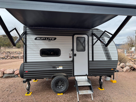This Sun Lite travel trailer, a great rv rental option, is set up at a campsite with its awning extended and LED lights on.