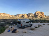 RV rental camper van parked among iconic Joshua Trees and rock formations, ready for desert adventures.