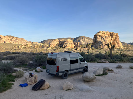 RV rental camper van parked among iconic Joshua Trees and rock formations, ready for desert adventures.