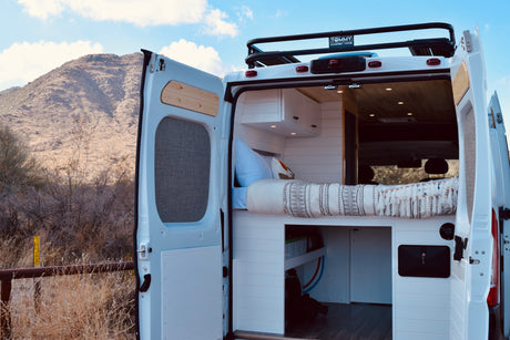 RV rental-ready custom camper van interior with a cozy bed, storage, and modern design, parked in a desert landscape.