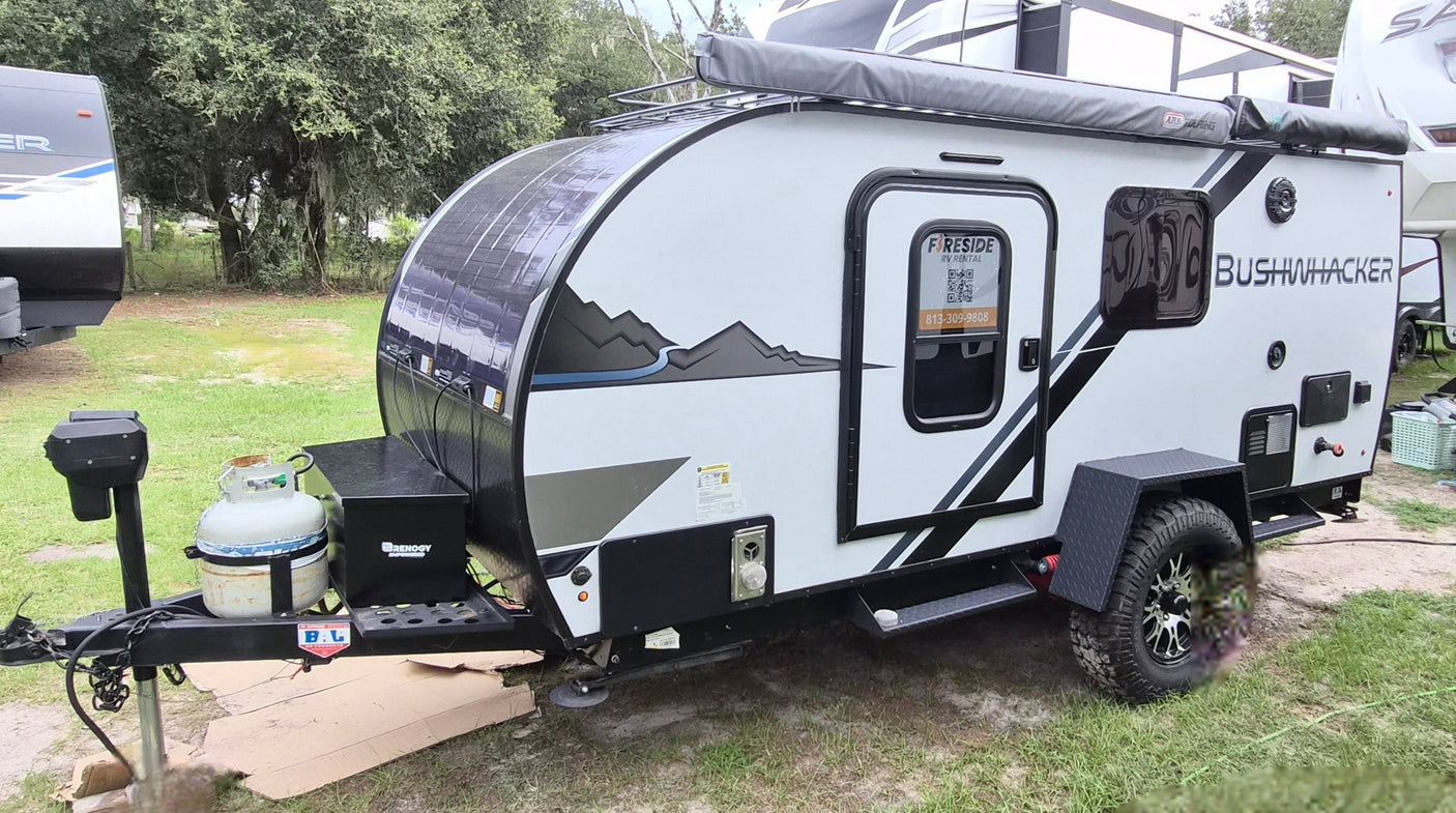 Bushwhacker teardrop RV rental, a rugged travel trailer with awning & off-road tires, parked on grass.
