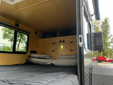 RV rental interior featuring a cozy bed, overhead storage, and a window offering a scenic outdoor view.