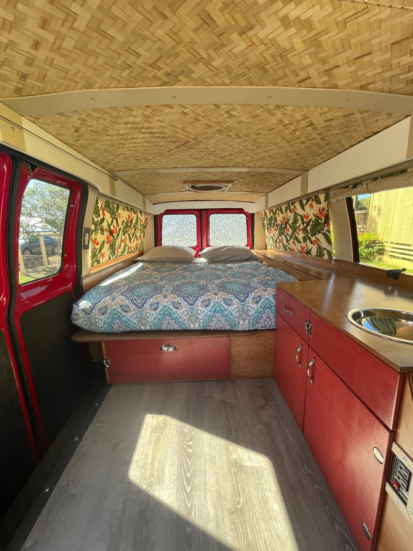 This inviting RV rental interior features a woven ceiling, comfy bed, and a compact kitchen. Ready for your next adventure!