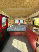 This inviting RV rental interior features a woven ceiling, comfy bed, and a compact kitchen. Ready for your next adventure!