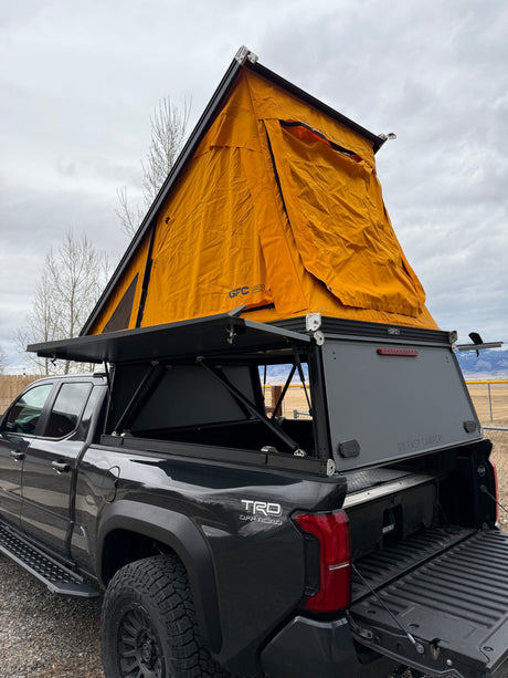 Dark gray Toyota Tacoma pickup with a GFC pop-up rooftop tent and open camper shell. Ideal for an RV rental adventure.