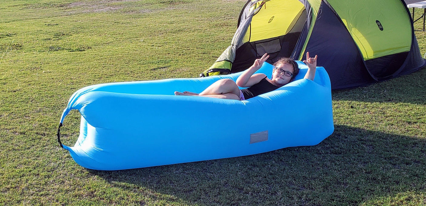 Young person enjoys a blue inflatable lounge chair by a green tent. Relaxing outdoors is ideal for your next RV rental adventure!