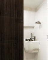 Compact RV rental bathroom: wall-mounted white sink, chrome faucet, and dark wood paneling.