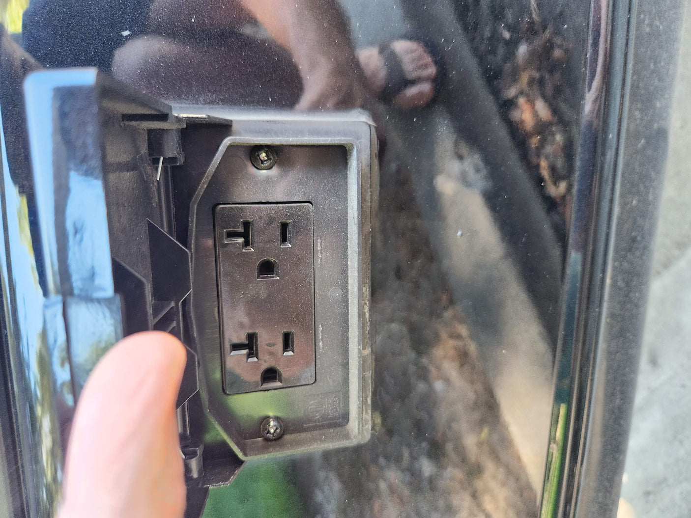 A finger reveals a heavy-duty outdoor 120V electrical outlet, ideal for an RV rental or campsite power hookup.