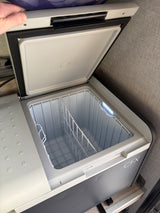 Open, empty Dometic CFX portable cooler in an RV rental, showing its wire basket and bright LED interior light.