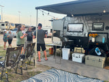 Friends gathered at an Opus off-road RV rental site, featuring an outdoor kitchen, string lights, and comfy chairs.