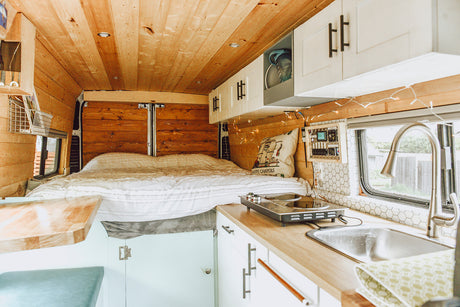 Explore this modern RV rental's inviting interior: wood accents, comfy bed, and kitchenette with sink/cooktop.