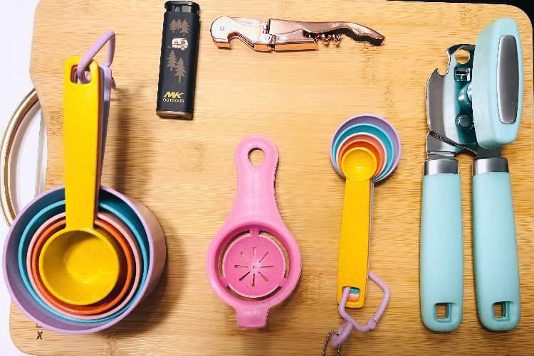 RV rental kitchen essentials: colorful measuring cups/spoons, can opener, corkscrew, egg separator, and lighter.
