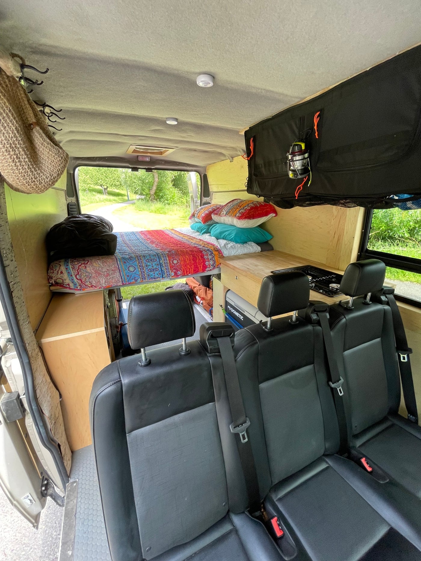  parked by trees & grass on a sunny day.|Cozy RV rental interior featuring a built-in bed with colorful pillows — photo 4