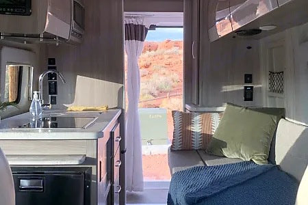 Inside a modern **rv rental**: a compact kitchen with sink and fridge, plus a cozy living area. Scenic red rock views outside.