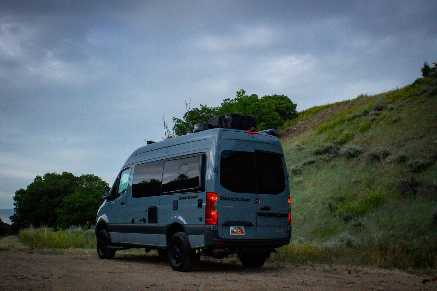 Gray "Sanctuary" Mercedes Sprinter camper van, perfect for your next RV rental adventure, parked on a dirt road.