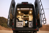 Rear view of an RV rental camper van, doors open, revealing a cozy, functional interior with a bed & table.