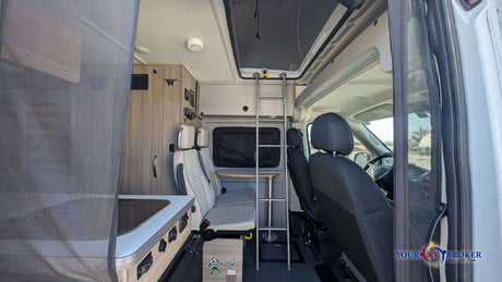 This RV rental interior features a kitchenette, dinette seating, and ladder to an overhead bunk, ready for adventure.