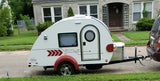 This compact white teardrop camper, perfect for an RV rental, is ready for travel, hitched to an SUV on a sunny street.